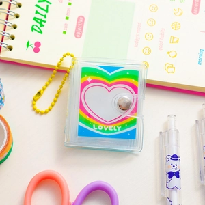 Close-up of a mini transparent PVC photo album with a rainbow heart card and yellow bead chain