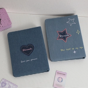 Detail of blue denim photocard binders with heart and star embroidery on striped surface