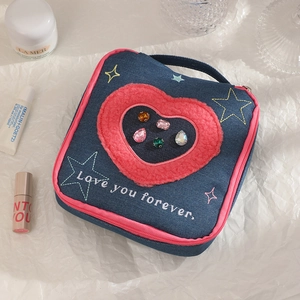 Top view of denim makeup bag with heart embroidery and colorful gems on white texture