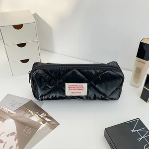 Detailed view of quilted black glossy pencil case with a label on a white desktop