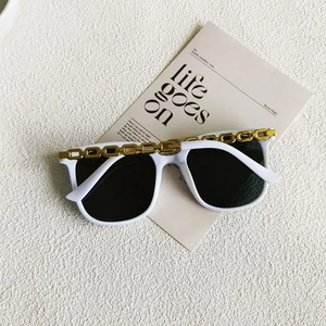 Detail einer weißen Oversize-Sonnenbrille mit goldener Metallkette am oberen Rahmenrand