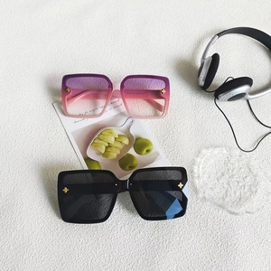 Detail of square oversized sunglasses featuring gold clover accents on gradient and black frames