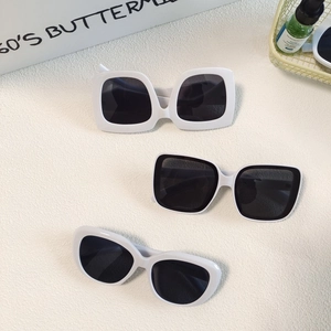 Three pairs of white oval and square sunglasses with dark lenses on a textured surface