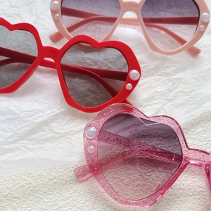 Detail von herzförmigen Kinder-Sonnenbrillen mit Perlenakzenten in Rot, Rosa und Glitzer-Lila