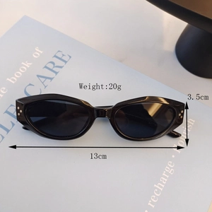 Detail view of black oval kids sunglasses with silver studs on a blue book with dimensions