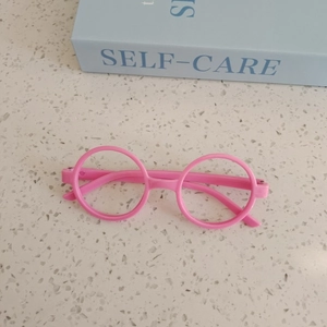 Pink round frame kids fashion glasses frame shown on a desk with decorative book