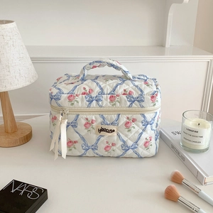 Détail de la trousse de maquillage matelassée aux motifs floraux et rubans aux zips