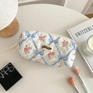 Trousse à maquillage matelassée aux motifs floraux et rubans bleus sur un bureau