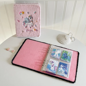 Close-up of pink plush photocard binder featuring unicorn embroidery and clear pocket sleeves