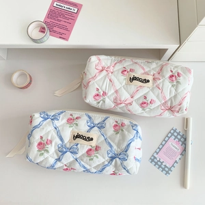 Close-up of quilted pencil cases with pink and blue floral bow patterns on a desk