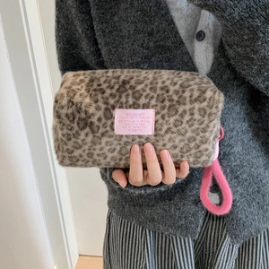 Plush leopard print makeup bag with pink hand strap and woven label held by a model