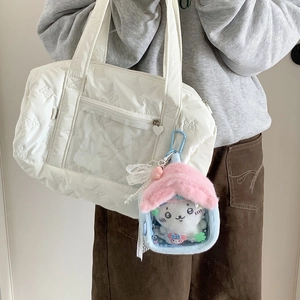 Detail of plush house-shaped doll display bag hanging on a quilted white handbag