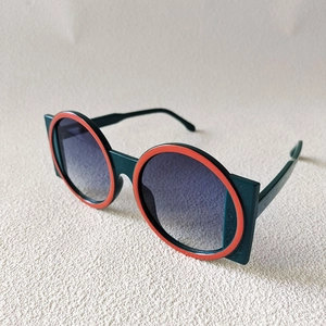 Detail view of bold round sunglasses with dark green frames and orange accent rings