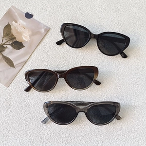 Retro cat-eye sunglasses in black, brown, and gray on textured background with white roses