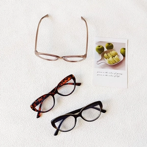 Three cat-eye glasses frames in tortoise, clear brown and black on a white textured base