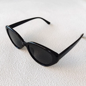 Top-down view of black cat-eye sunglasses with polished oval frames on white texture
