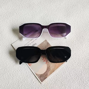 Détail de lunettes de soleil carrées avec montures blanches et noires sur fond texturé
