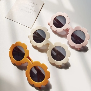 Three flower-shaped polarized kids sunglasses in pink, beige and yellow on a table