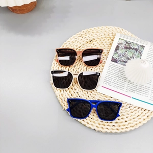 Detail view of square polarized kids sunglasses in orange, beige and blue on a straw mat