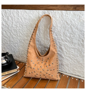 Detail of silver rivets on brown suede hobo tote bag against white wall background