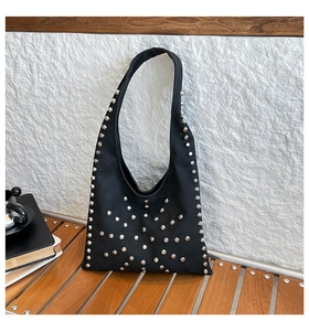 Detail shot of black suede tote bag with silver metal studs on a wooden surface