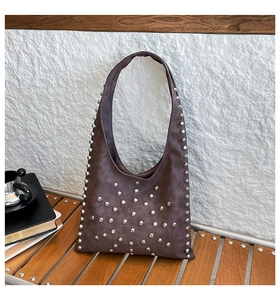 Detail of silver rivets on a brown suede hobo bag placed on a dark wooden bench