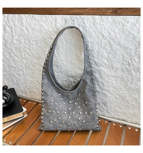 Detail of gray suede bucket bag featuring metallic rivets and stylish curved handle