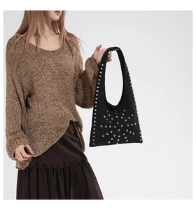 Detail of black tote bag with silver rivets held by a model in a retro outfit
