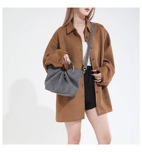 Detail view of dark grey pleated cloud handbag with metal ring handles and brown shirt
