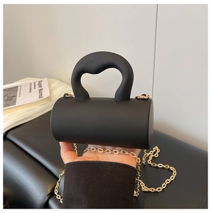 Détail du mini sac cylindrique noir avec poignée ondulée et bandoulière chaîne dorée