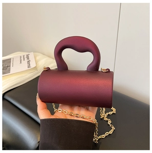 Détail du mini sac cylindre bordeaux mat avec une bandoulière en chaîne dorée
