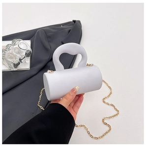 Gros plan d'un mini sac cylindrique blanc avec anse épaisse sur un blazer gris chic