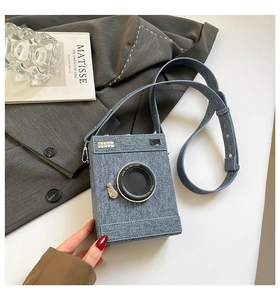 Detail of light blue denim camera-shaped crossbody bag with adjustable strap and lens decor