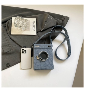 Detail view of retro camera-shaped blue denim crossbody bag on minimalist white table