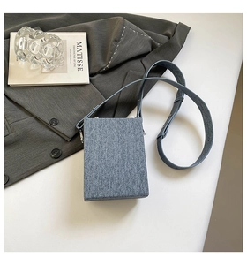 Detail of blue denim vertical rectangular crossbody bag on dark grey suit and art book