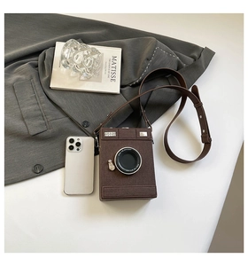 Detail of camera-shaped crossbody bag featuring textured brown leather and lens decor