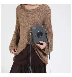 Detail of creative camera-shaped crossbody bag featuring textured fabric and leather strap