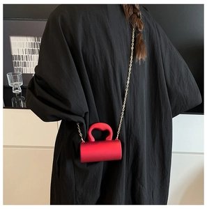 Détail du sac cylindrique rouge en acrylique avec poignée ondulée et chaîne dorée