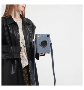 Detail view of a blue denim vintage camera-shaped crossbody bag worn by a female model