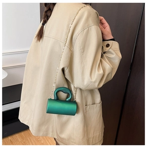 Vue détaillée du sac de soirée cylindrique vert avec chaîne dorée porté par un modèle