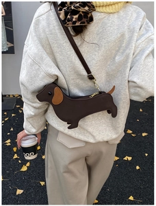 Brown dachshund shaped leather crossbody bag worn by a model in an autumn outdoor setting