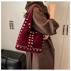 Gros plan d'un sac hobo en daim bordeaux avec rivets argentés porté sur un manteau marron