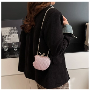 Detail of pink glitter apple-shaped crossbody bag with gold leaf clasp on a dark blazer