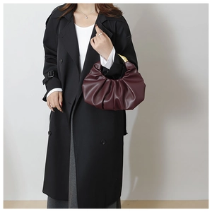 Detail of burgundy pleated handbag with gold metal handle styled on a black long coat