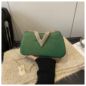 Detail of green luxury evening bag featuring sparkling texture and gold rhinestone V-buckle