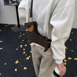 Creative dachshund-shaped crossbody bag in dark brown leather worn by a model outdoors