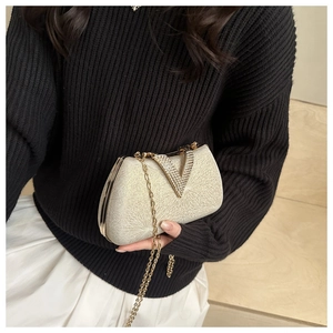 Detailed view of rhinestone V-shaped hardware and pleated texture on beige evening clutch