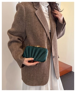 Detail of dark green pleated clutch bag with gold chain worn by model in suit