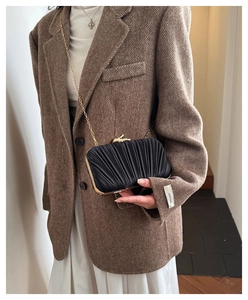 Detail of black pleated clutch with gold animal clasp and chain strap on model