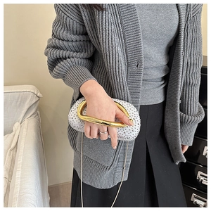 Detail of white rhinestone evening clutch bag with gold ring handle and metal chain strap